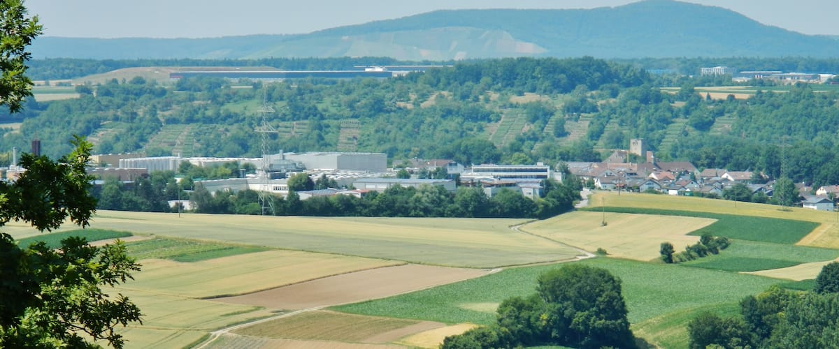 A rural landscape with fields, a small town, and distant mountains.