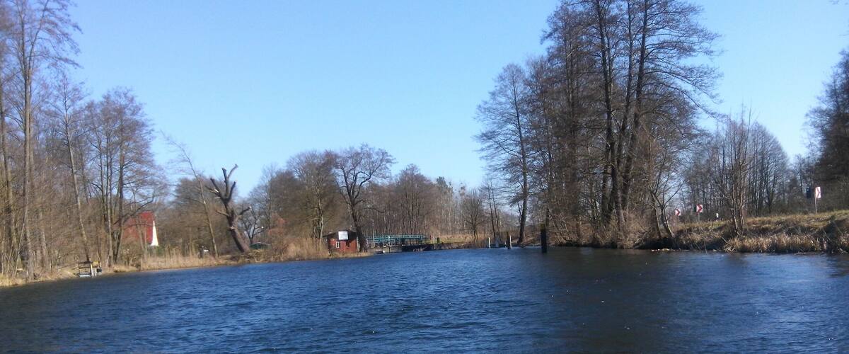 A river with trees and a red building on the left.