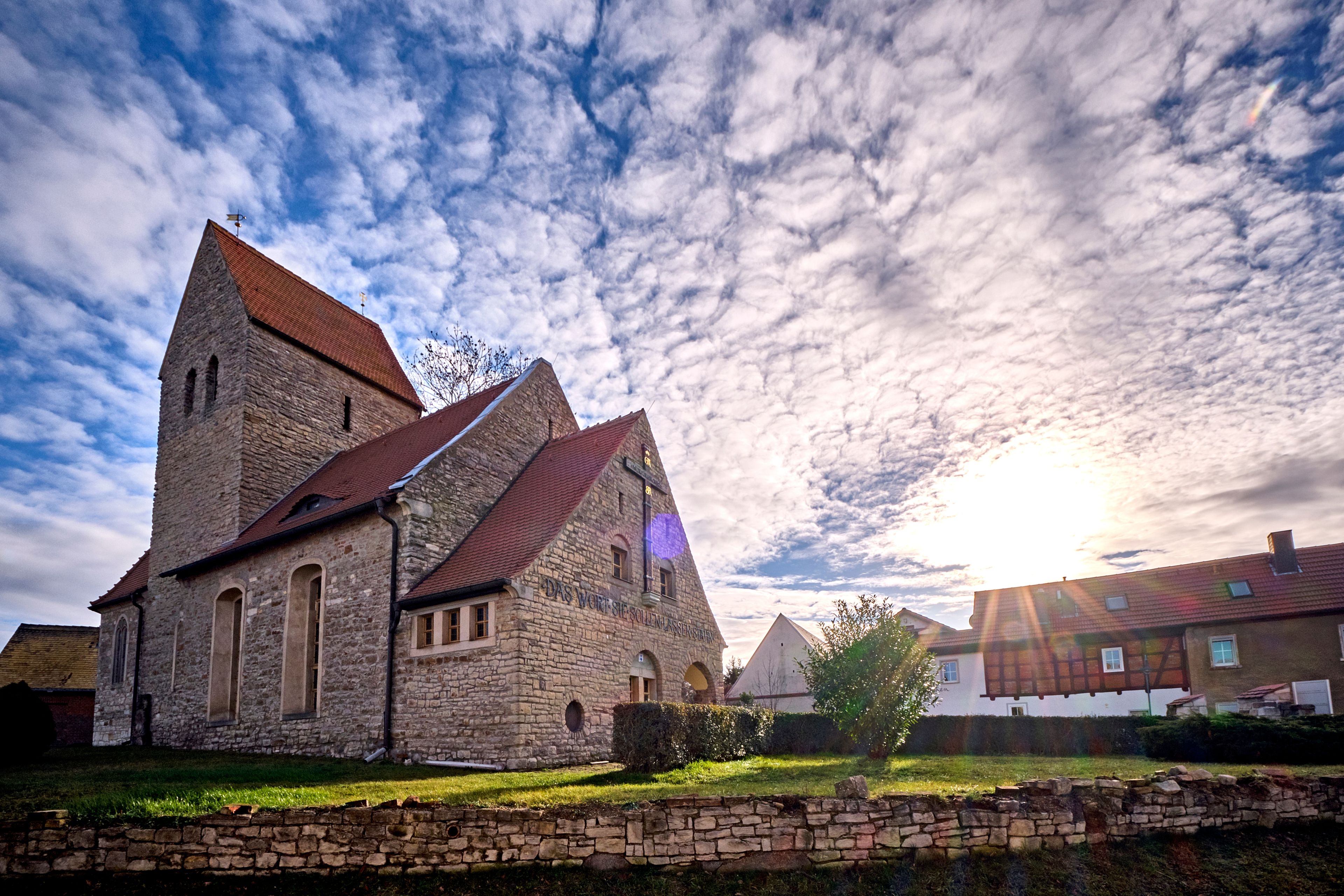 A stone church with a red roof and a clear sky with clouds.