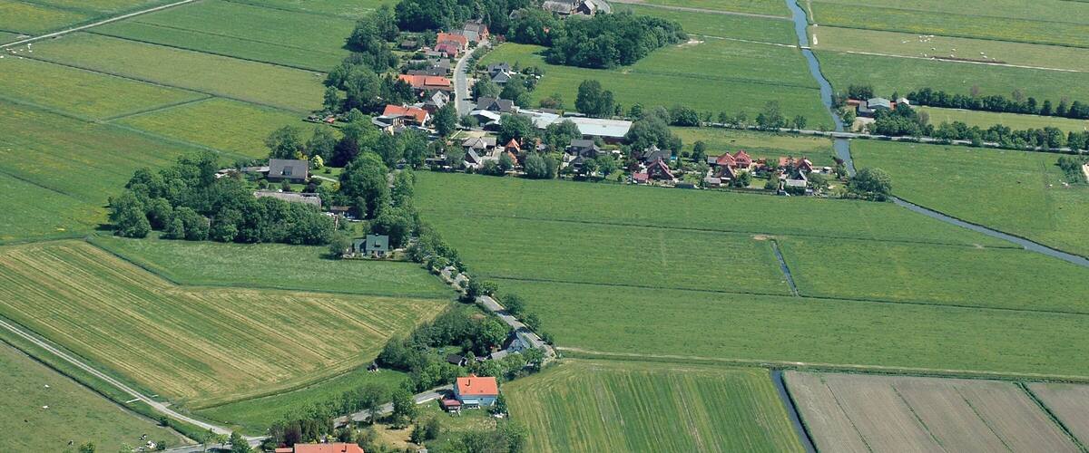 An aerial view of a rural village with fields, a river, and scattered houses.