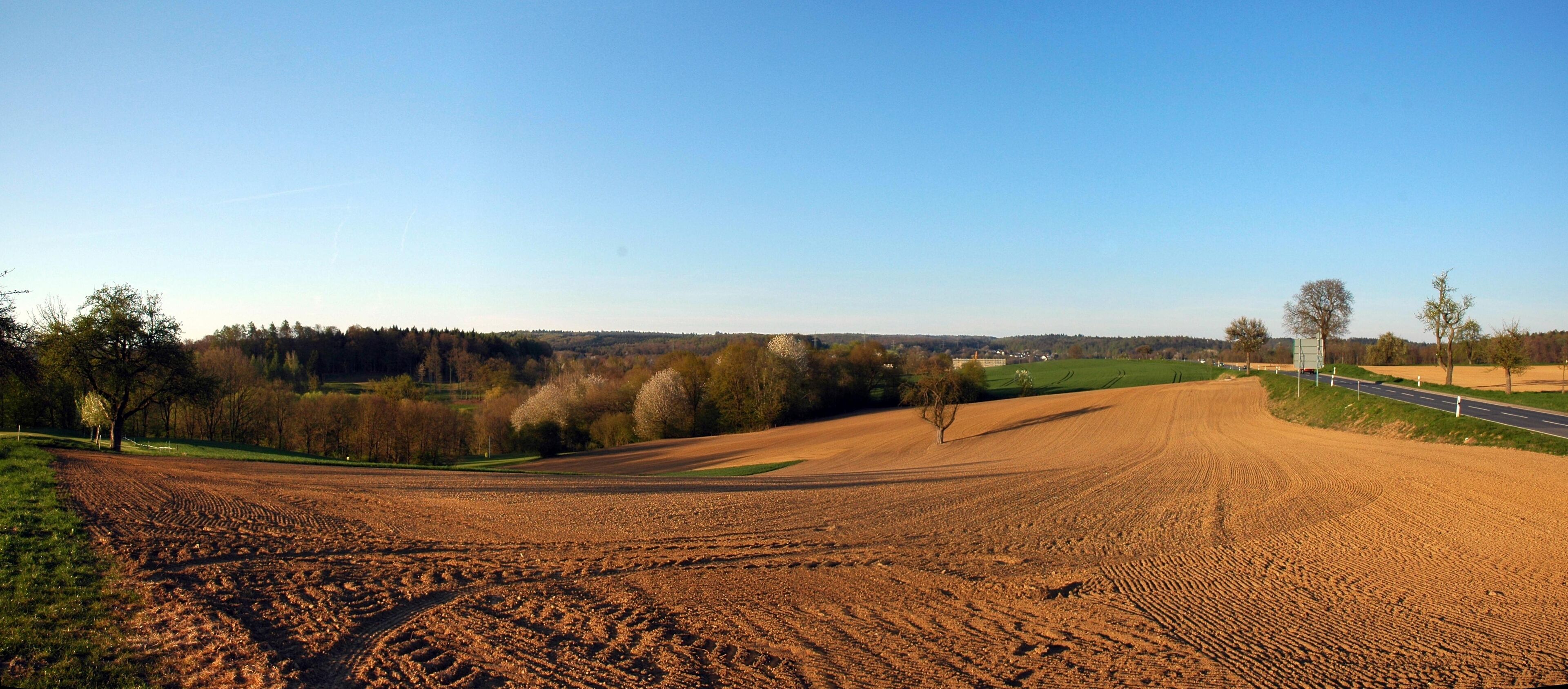 A plowed field with a road and trees in the background.