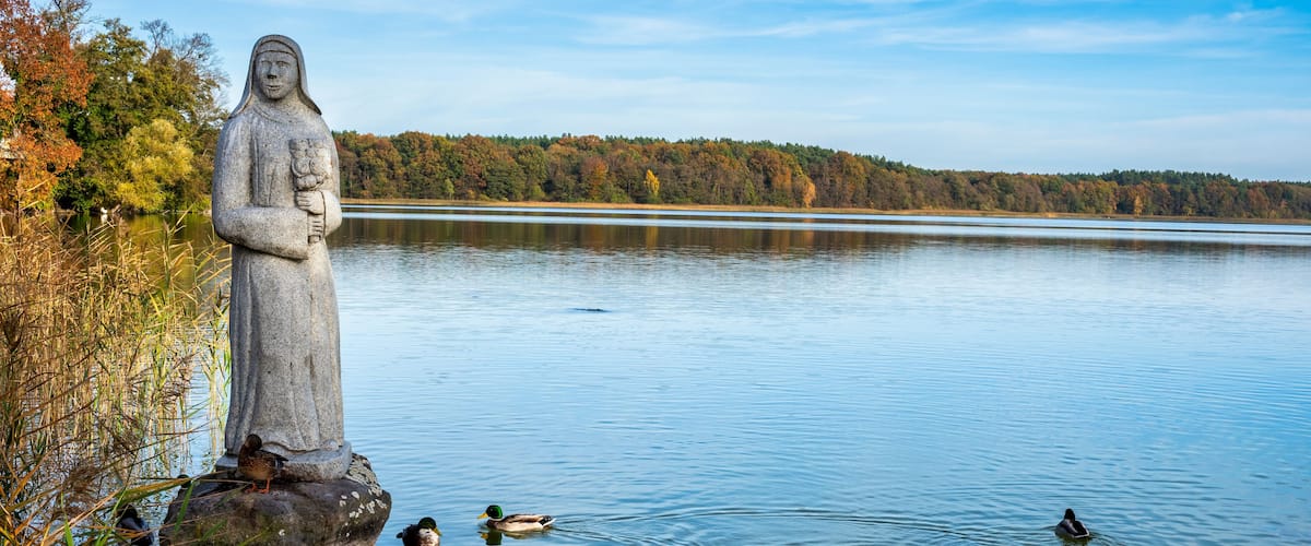 A statue by a calm lake with ducks swimming nearby.