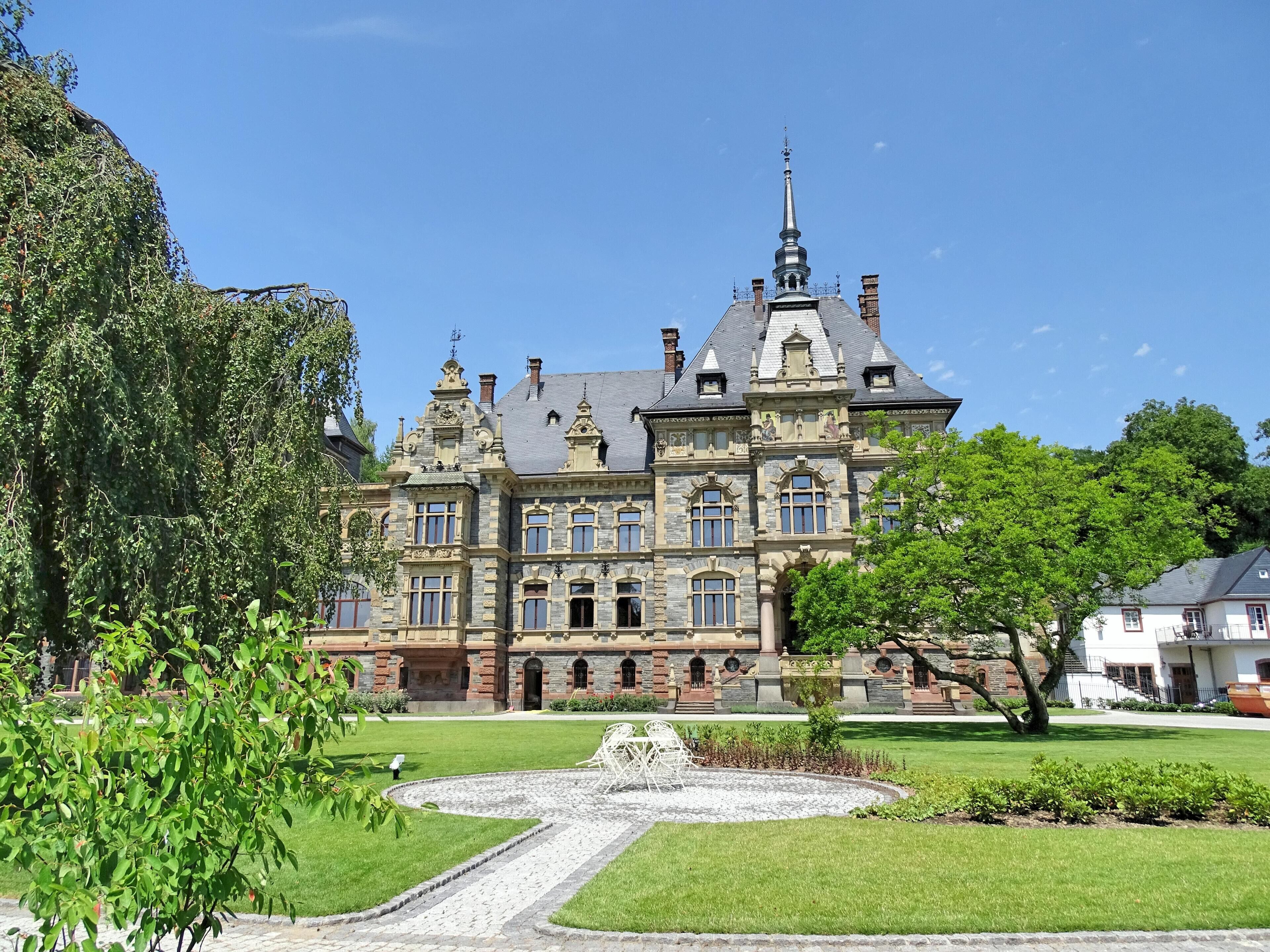 A large, ornate building with a prominent tower and a well-manicured garden in front.