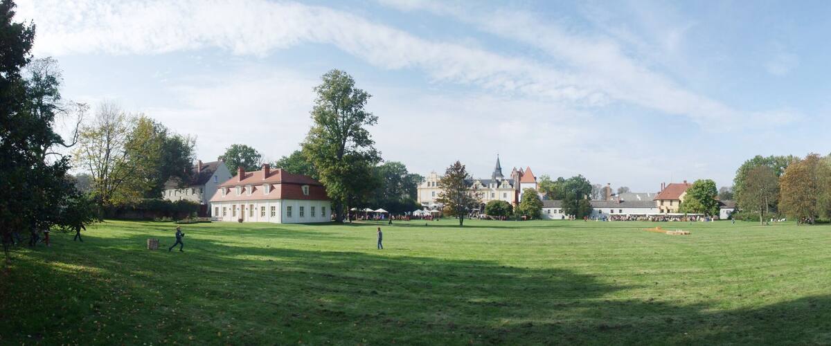 A large grassy field with a historic building and trees in the background.