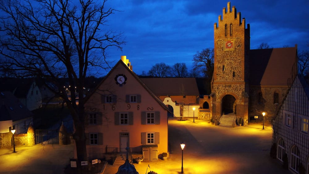 A historic town square at dusk with a prominent clock tower and traditional buildings.