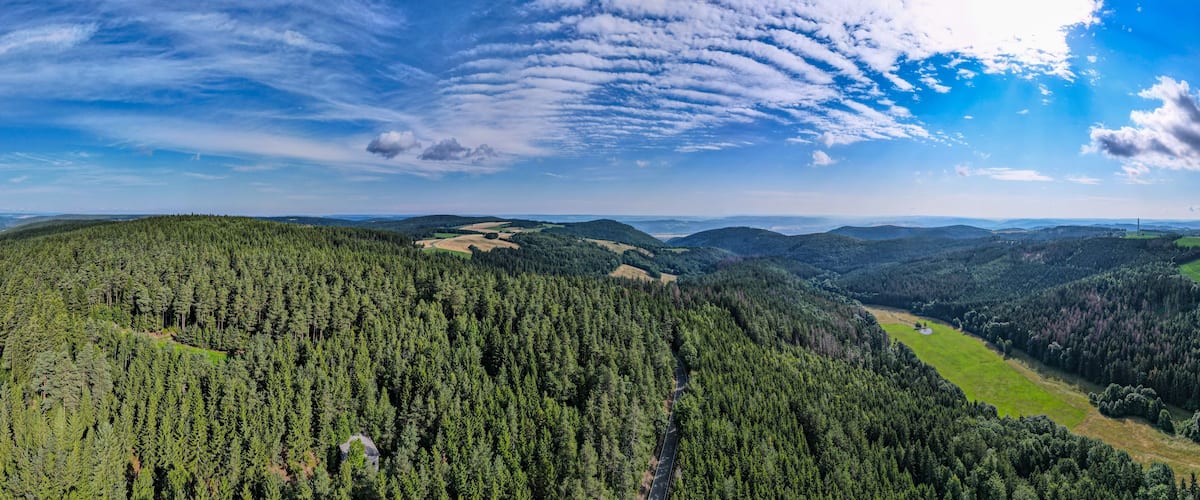 Un paysage montagneux boisé, avec une route sinueuse et des collines à l’horizon.