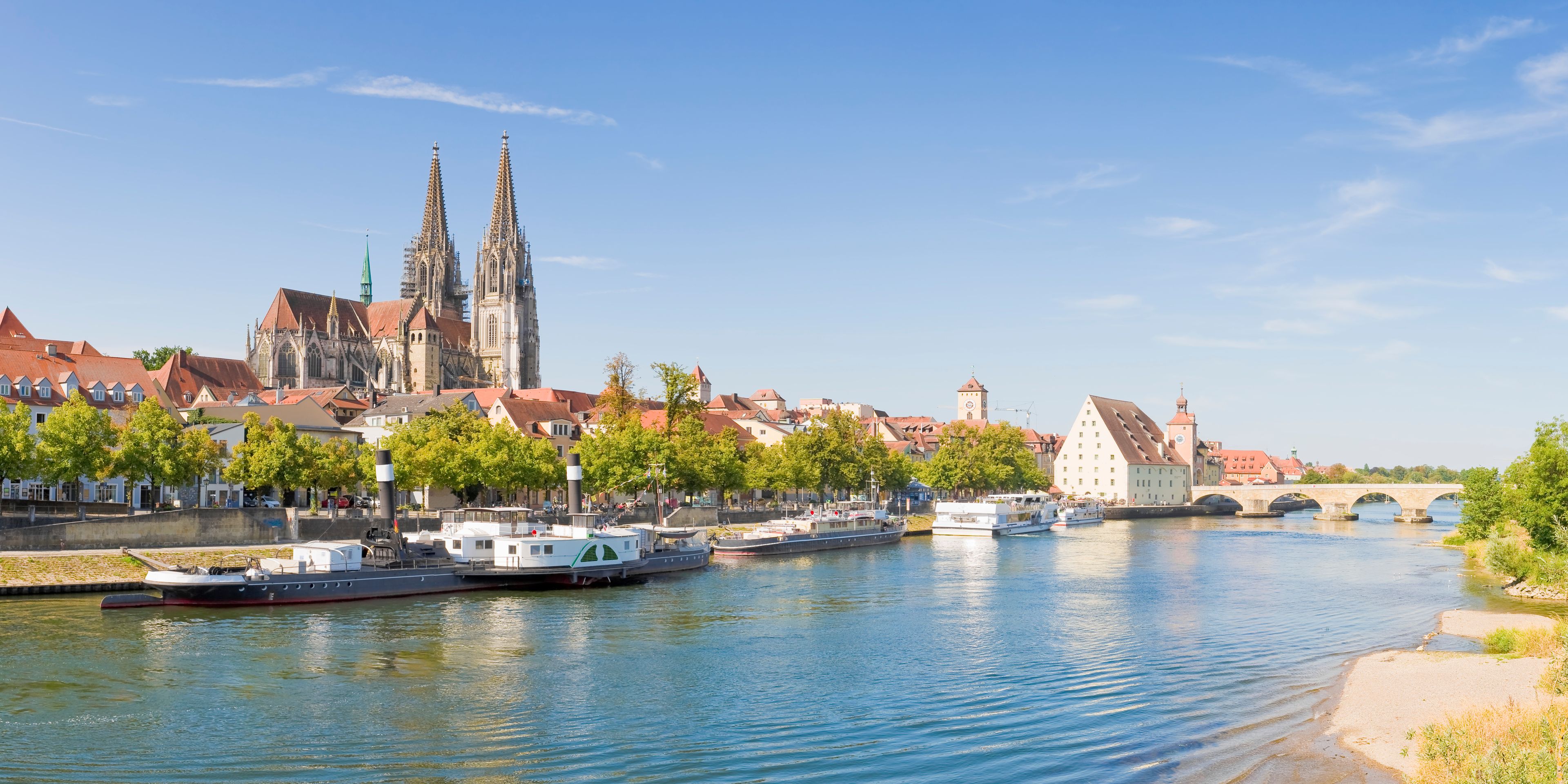 Un río con barcos, un puente y edificios históricos, incluyendo una catedral con dos torres.
