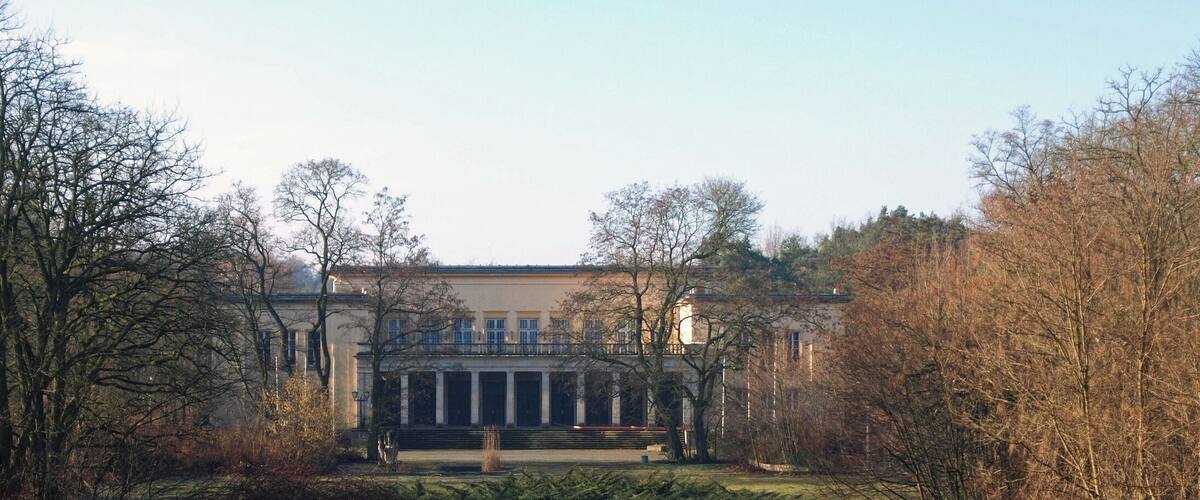 A large building with columns, surrounded by trees and a grassy field.