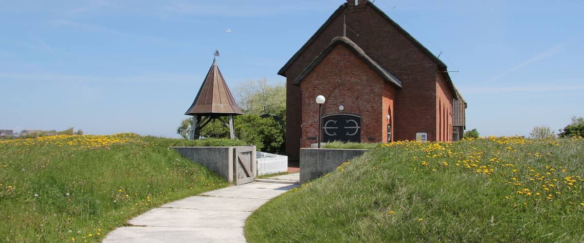 A brick church with a steeple and a smaller chapel in a grassy field.