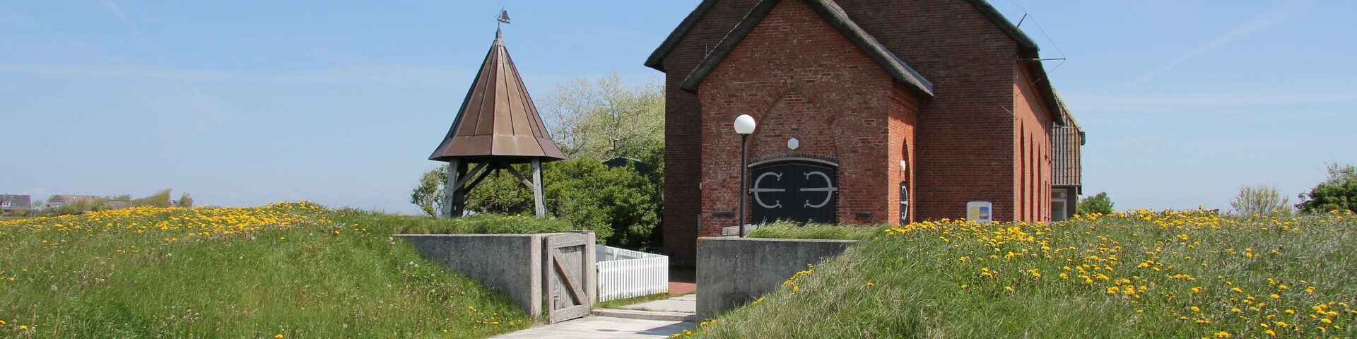 A brick church with a steeple and a smaller chapel in a grassy field.