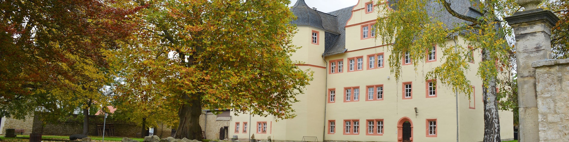 A large building with a stone wall and a bench in front.