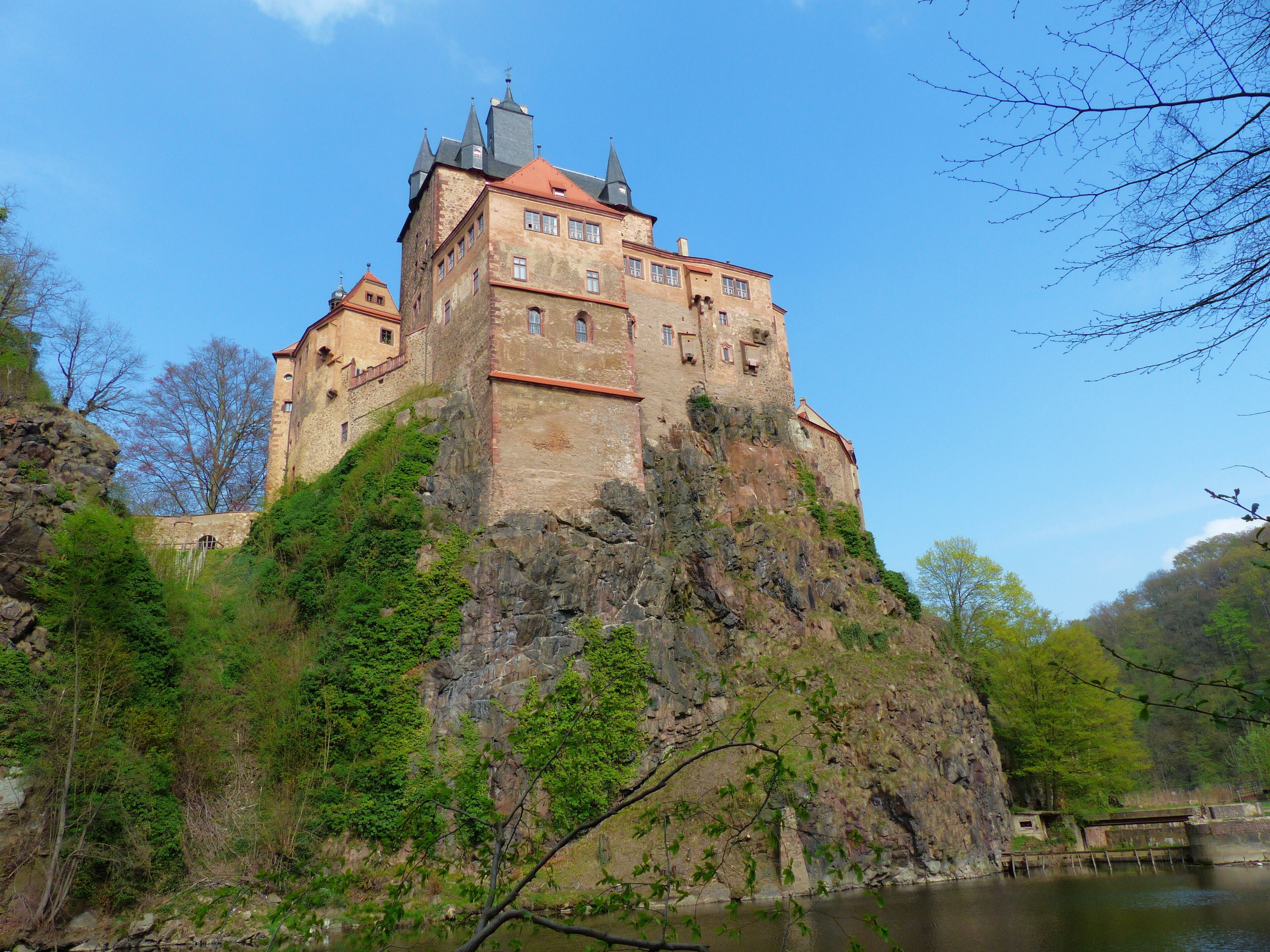 A castle on a rocky hill with a river in the foreground.