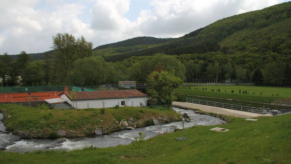 A river flowing through a green valley with a small building and a bridge.