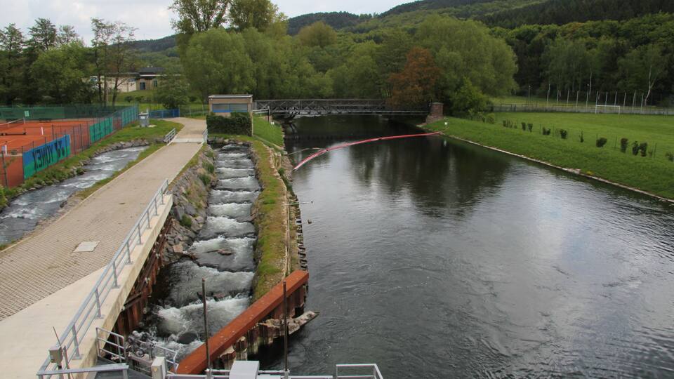 A river with a bridge, a dam, and a tennis court.