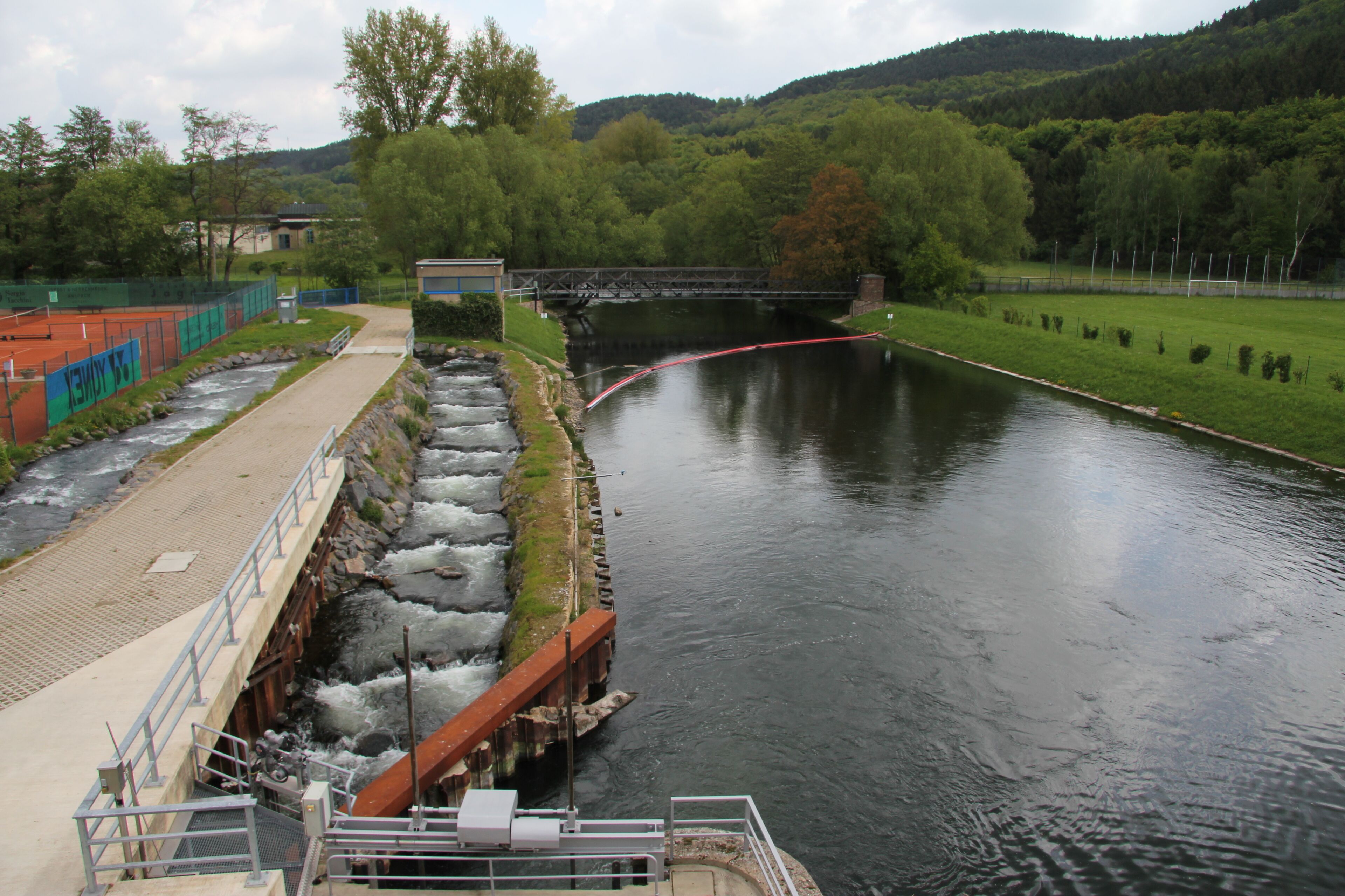 A river with a bridge, a dam, and a tennis court.