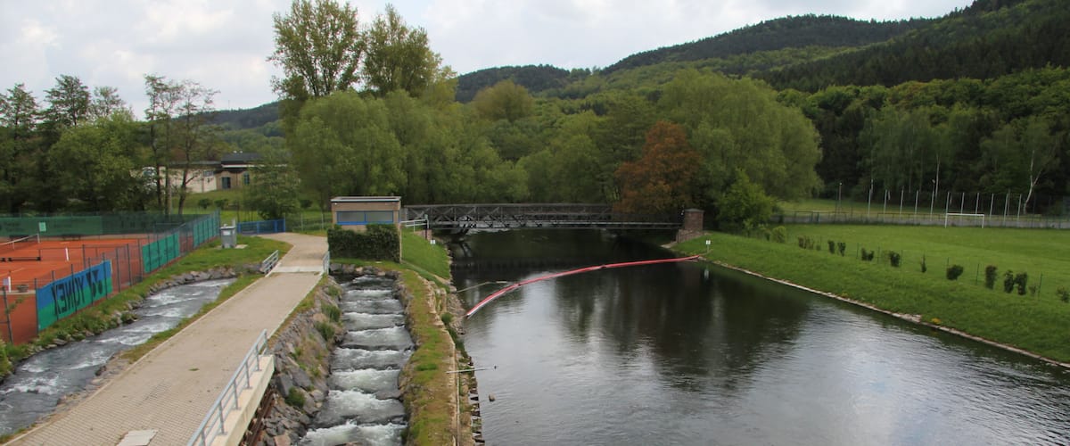 A river with a bridge, a dam, and a tennis court.