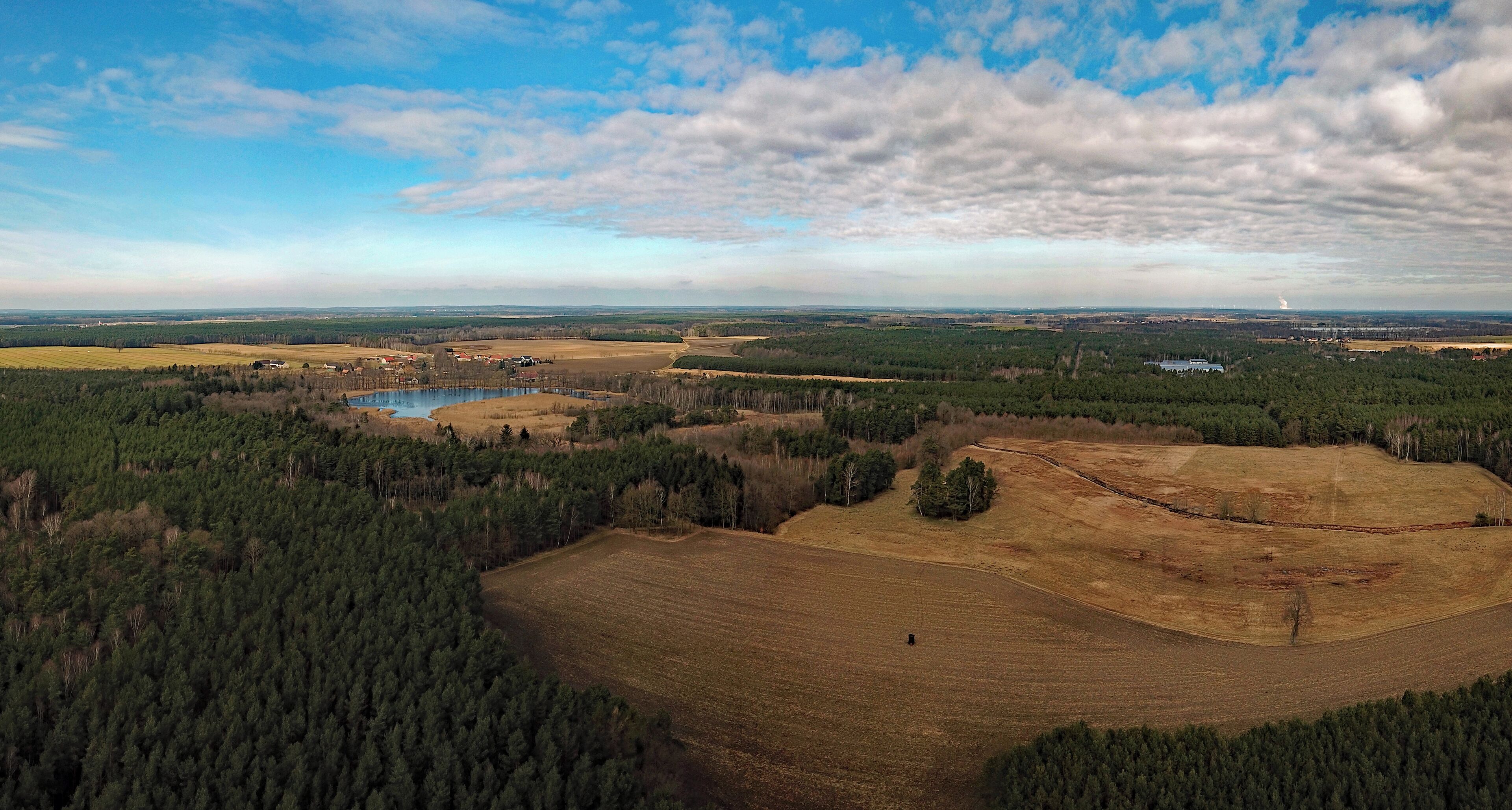 A rural landscape with a lake, dense forests, open fields, and distant buildings.