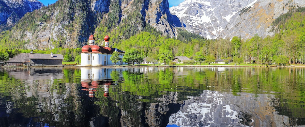 A mountain lake with a church and buildings reflected in the water.