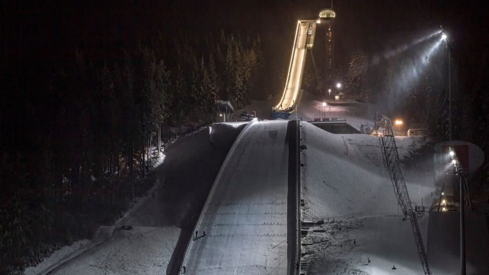 A snow-covered slope with a ski lift and artificial lighting at night.