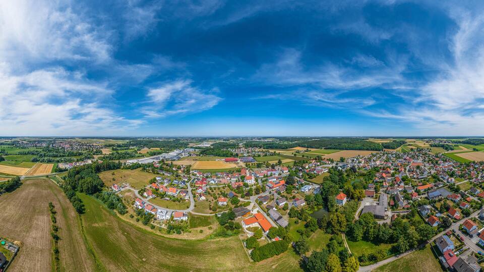 A panoramic view of a town surrounded by fields and forests under a clear sky.