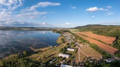 A lakeside village with boats, a dock, and surrounding fields.