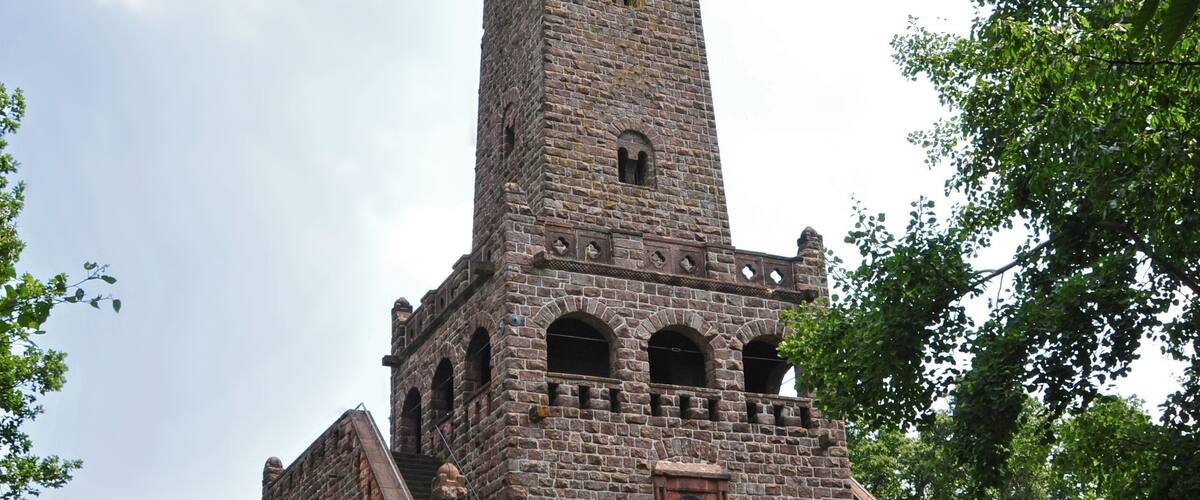 A tall stone tower with a clock and antenna, surrounded by trees.