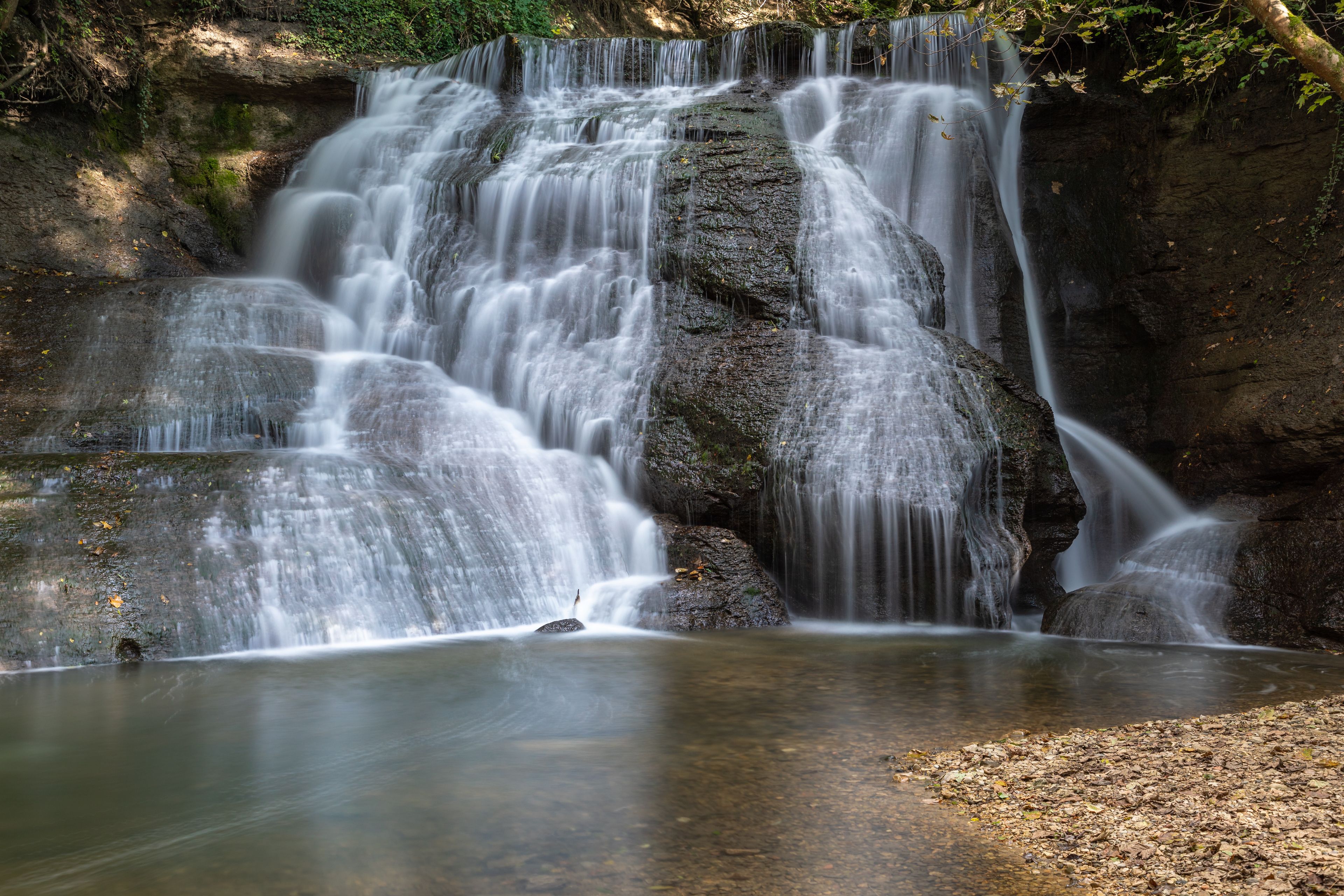 Una cascada fluye sobre rocas en un área boscosa.