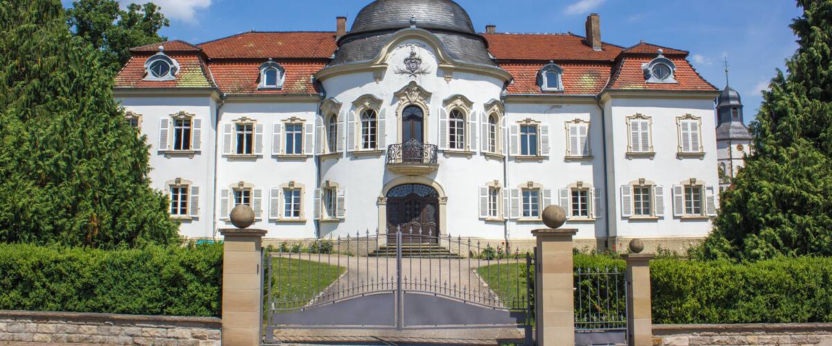 A large, white building with a dome and red-tiled roof, surrounded by greenery.