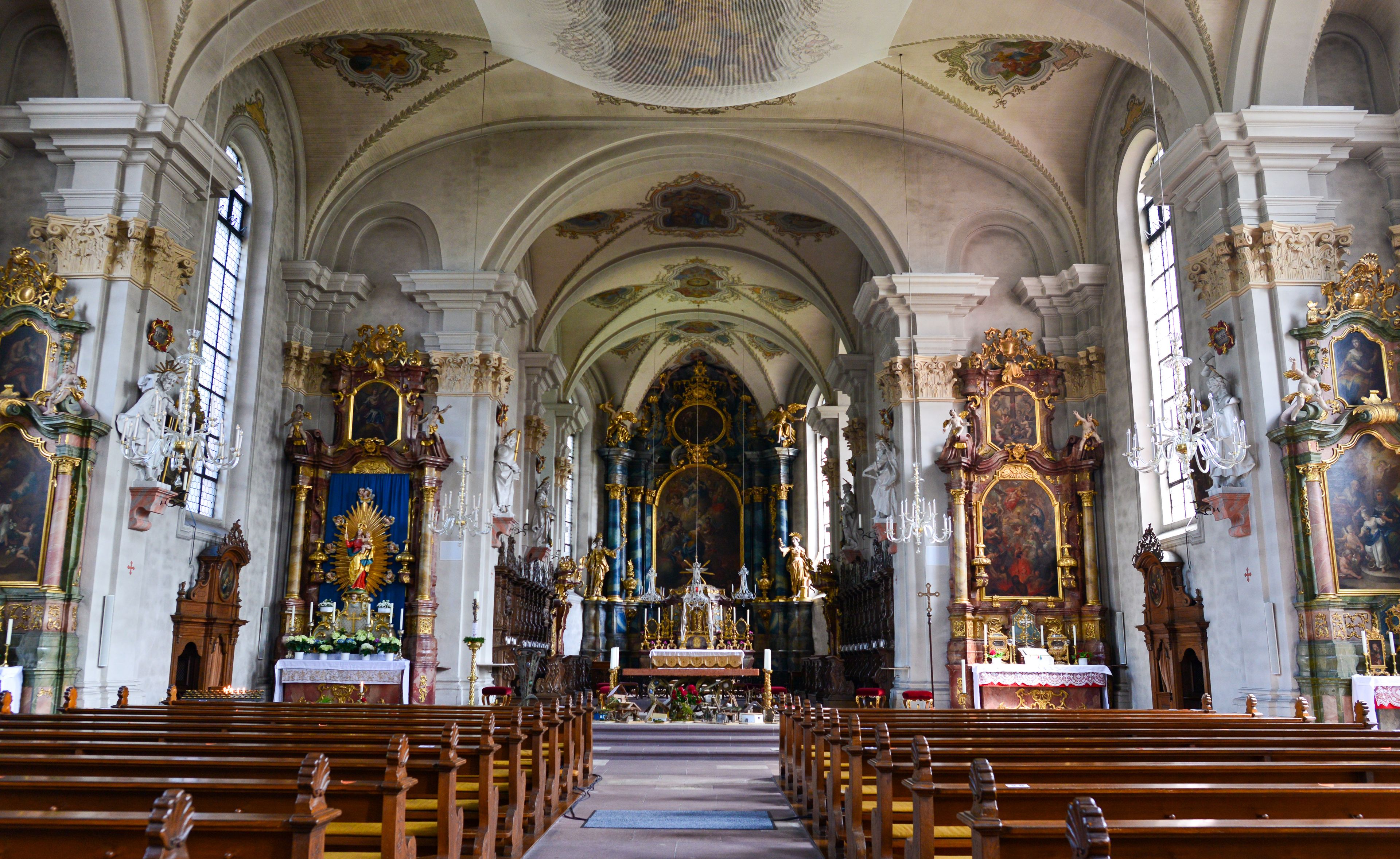 Een versierd kerkinterieur met hoge plafonds, gedetailleerde fresco's en een centraal altaar.