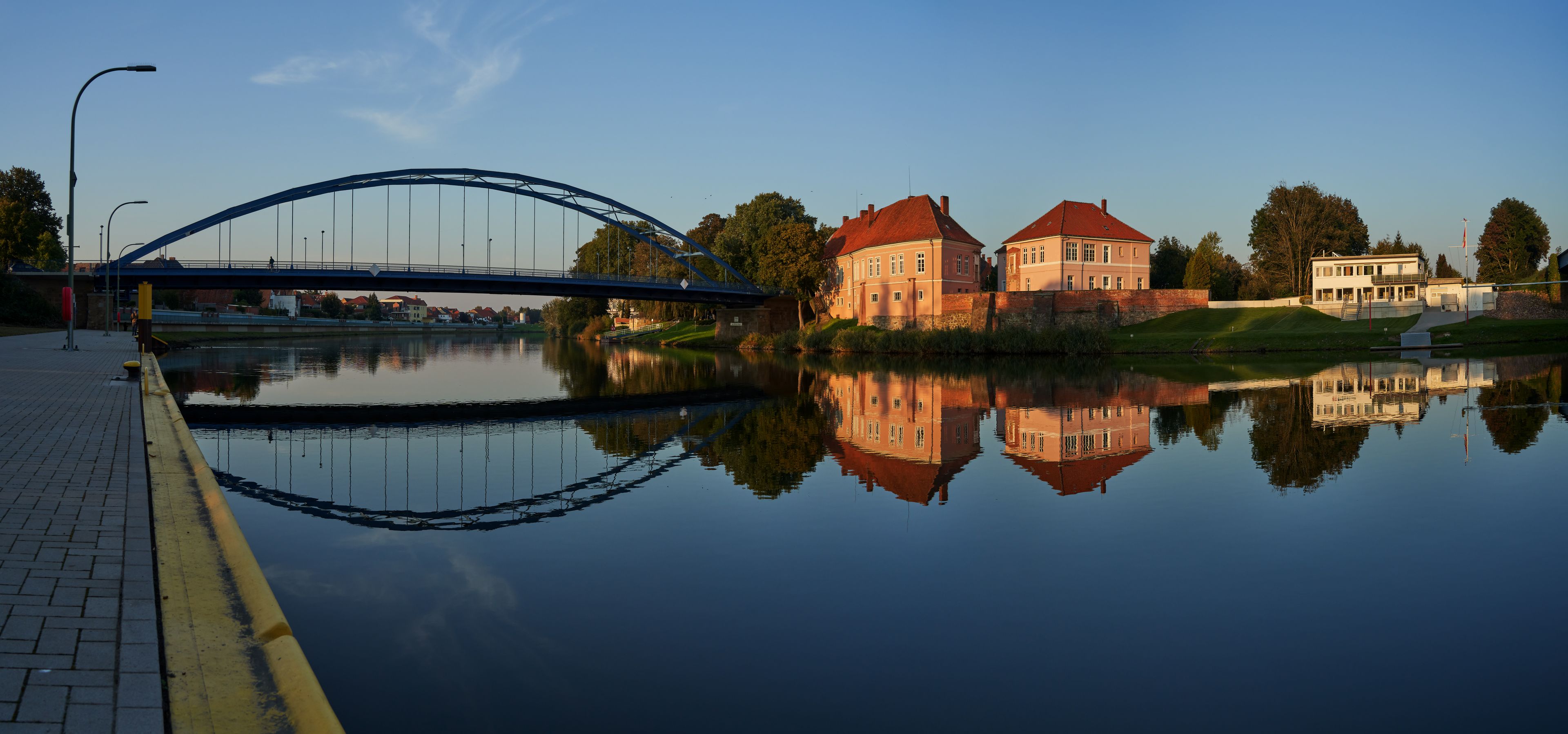 Hoya, Germany - October 10, 2021: panorama of the river Weser with the former duke's castle and the road bridge reflecting in the tranquil water during the golden hour