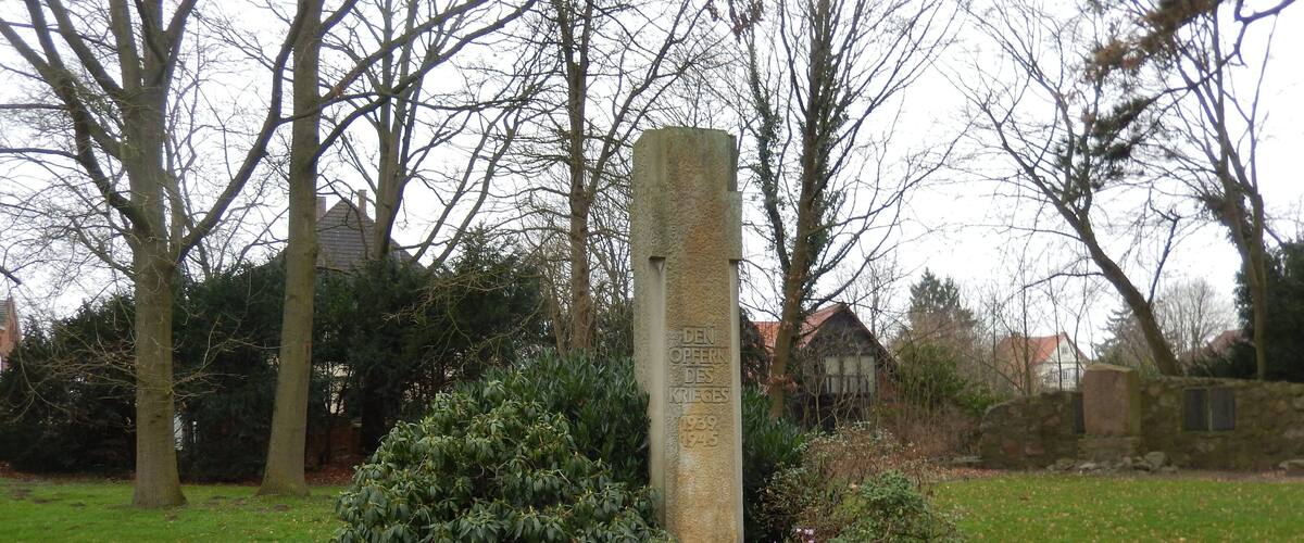 A gravestone in a grassy area with trees and a stone wall in the background.