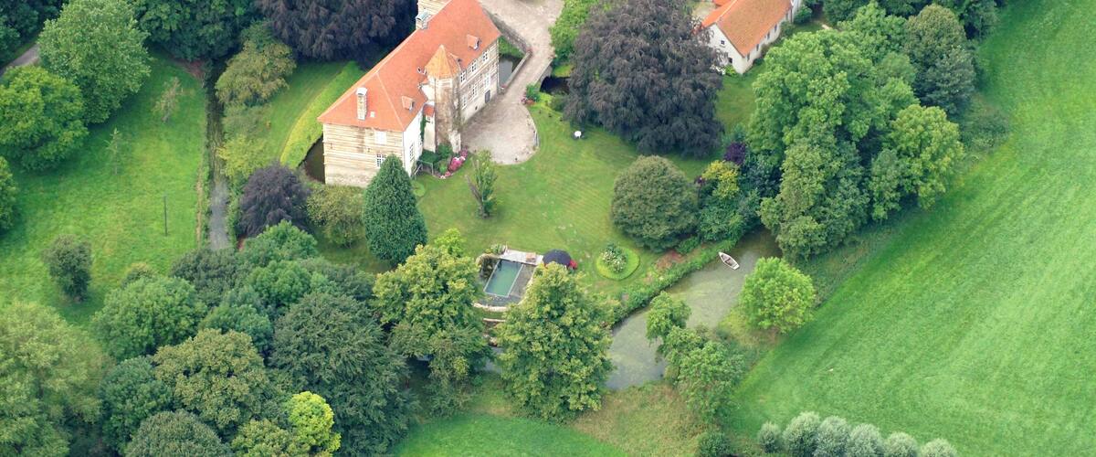 An aerial view of a large estate with multiple buildings, surrounded by lush greenery and trees.