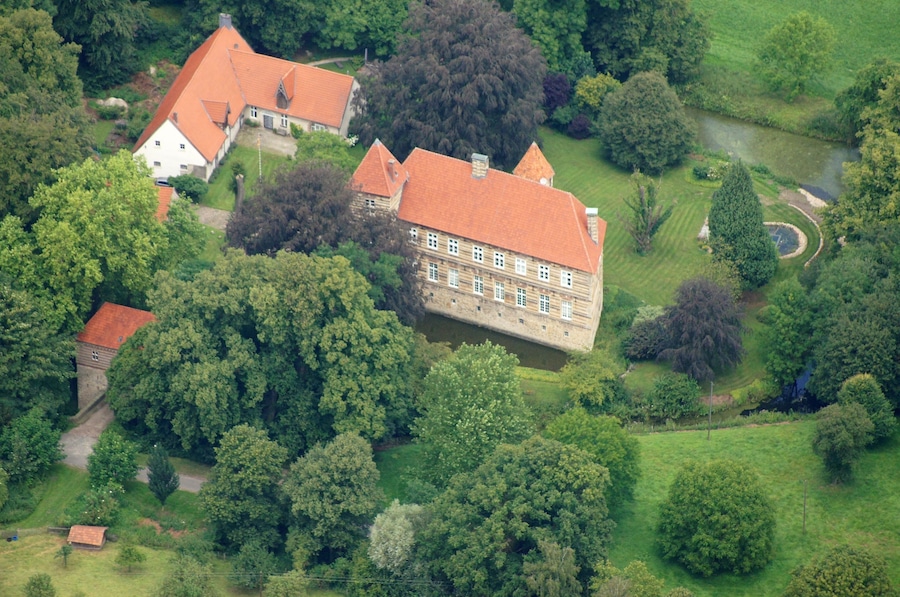An aerial view of a large estate with a prominent red-roofed building surrounded by lush greenery and a small pond.