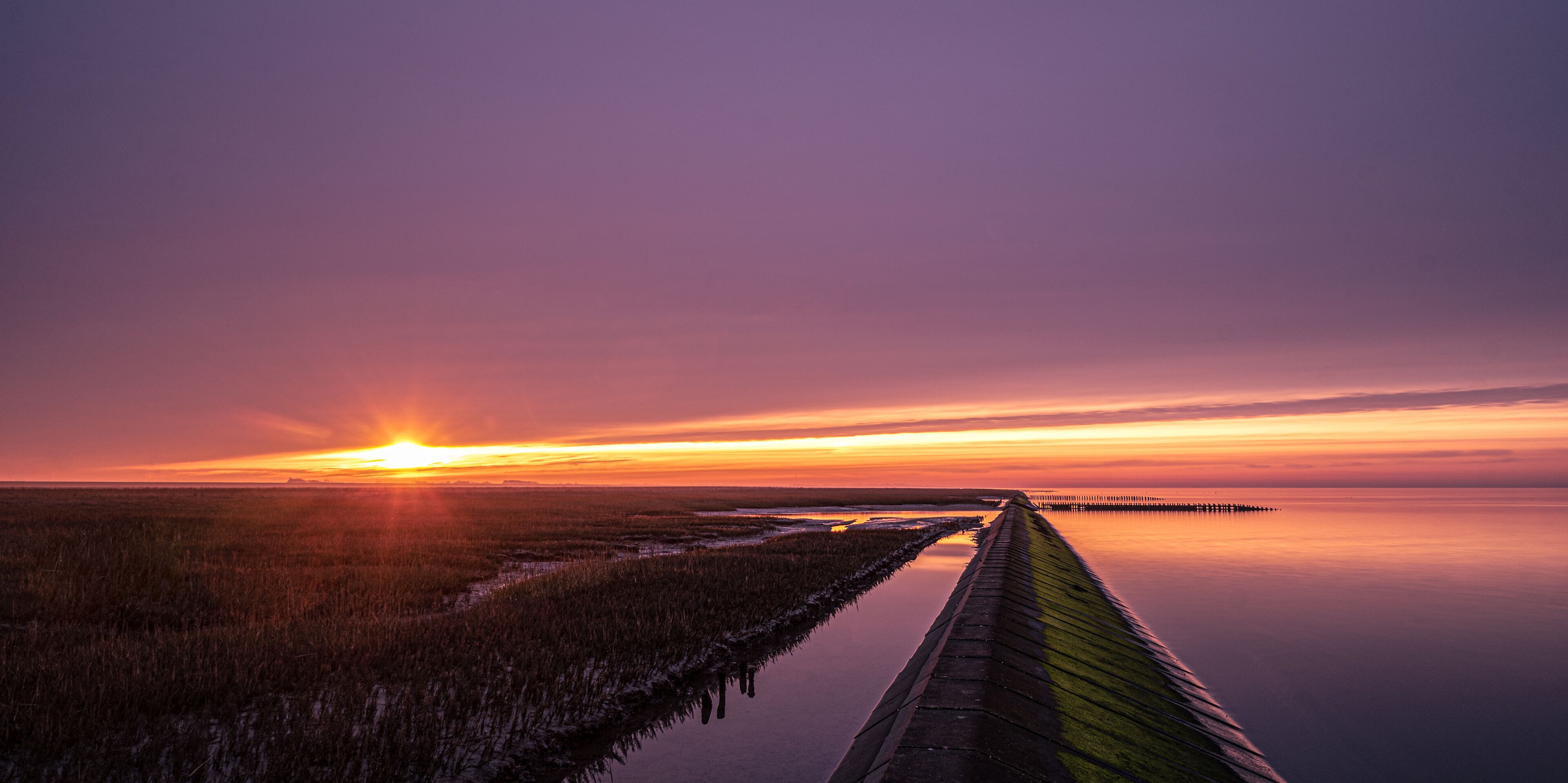 A sunset over a calm water body with a long pier extending into the water.