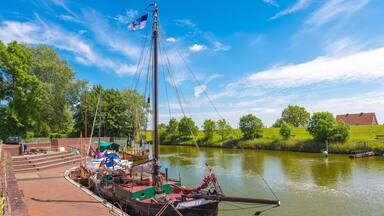 A river with a docked boat, a grassy bank, and a clear blue sky.
