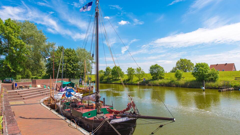 A river with a docked boat, a grassy bank, and a clear blue sky.