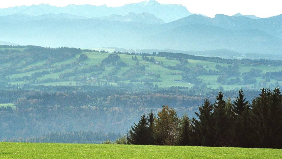Rolling green hills, a forested area, and distant mountains.