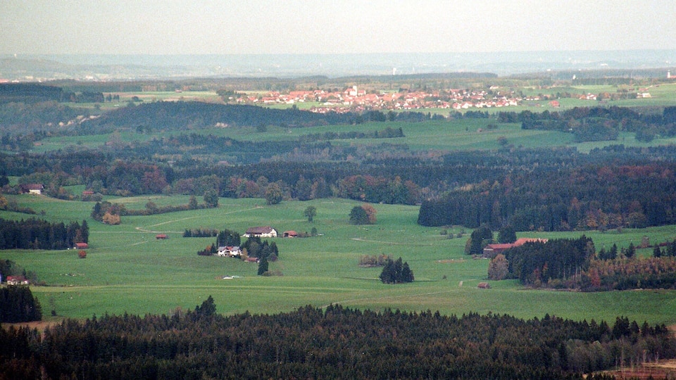 A rural landscape with rolling hills, scattered houses, and dense forests.
