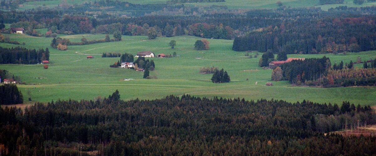 A rural landscape with rolling hills, scattered houses, and dense forests.