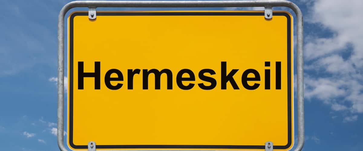 A yellow sign with the word "Hermeskeil" against a blue sky with clouds.