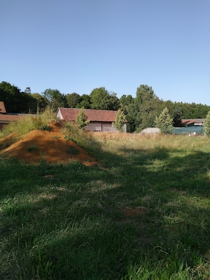 Un paysage rural avec une butte de terre, une grange au toit rouge et une construction au toit vert.