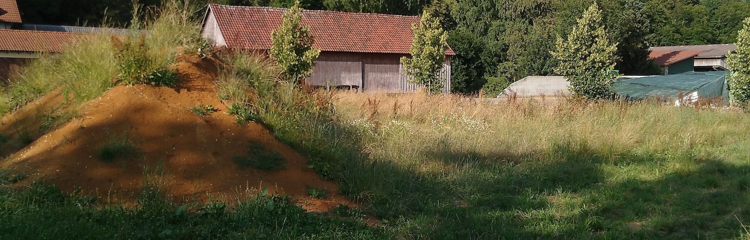 A rural landscape with a dirt mound, a red-roofed barn, and a green-roofed structure.
