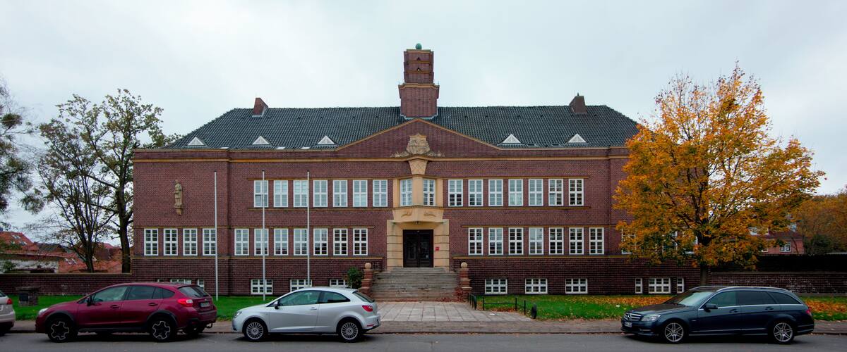 A large brick building with a central entrance, surrounded by cars and trees.