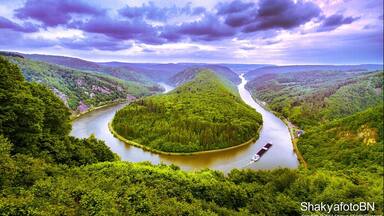 A river winding through a lush valley with dense greenery and a boat on the water.