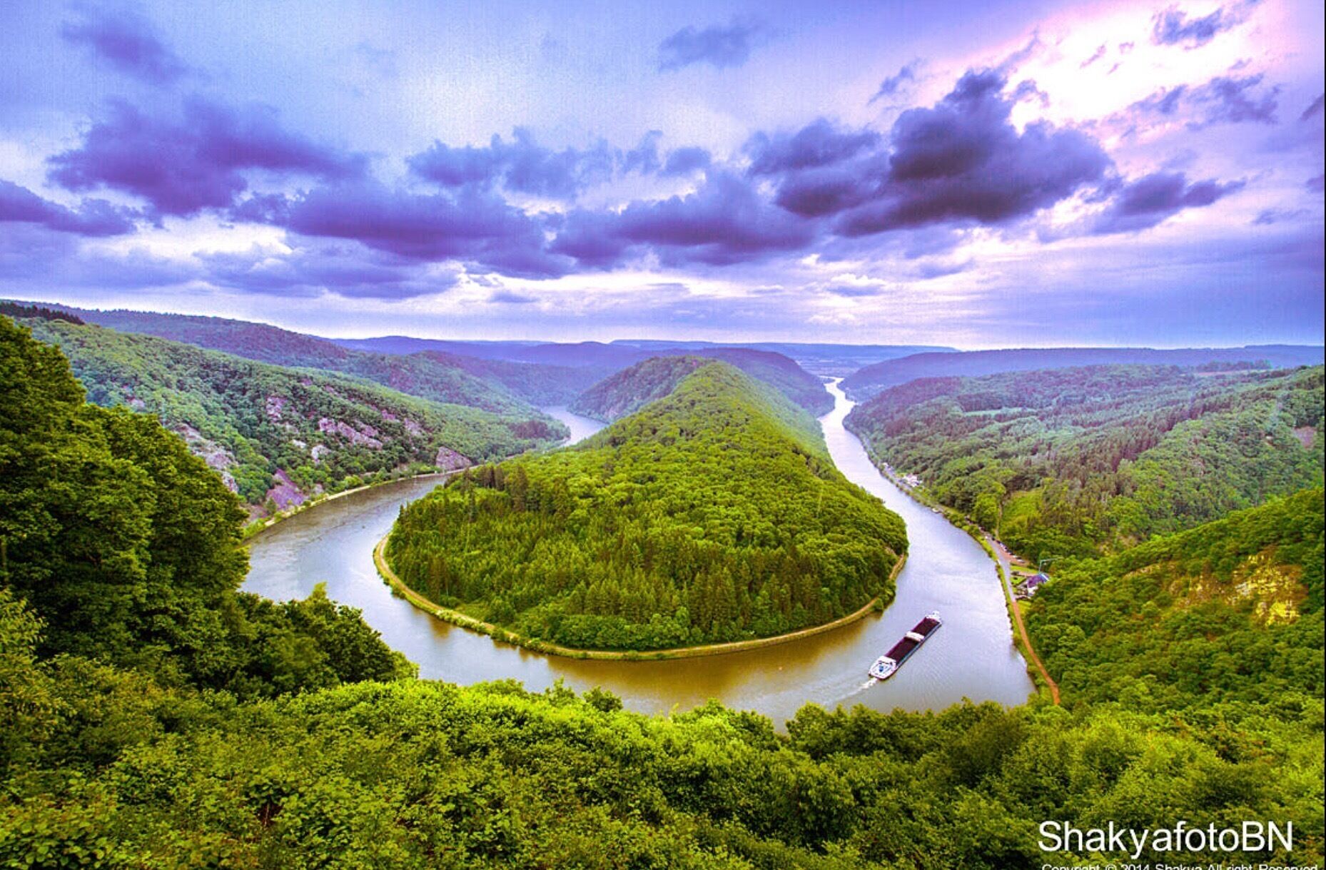 A river winding through a lush valley with dense greenery and a boat on the water.