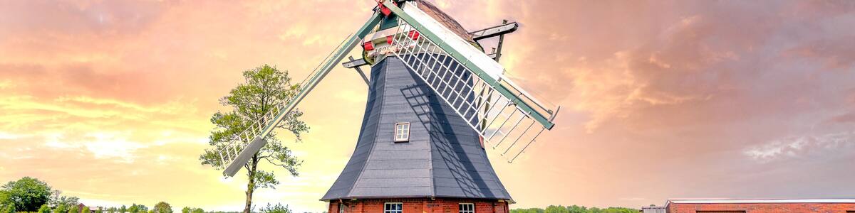 A traditional windmill with a white fence in a rural setting.