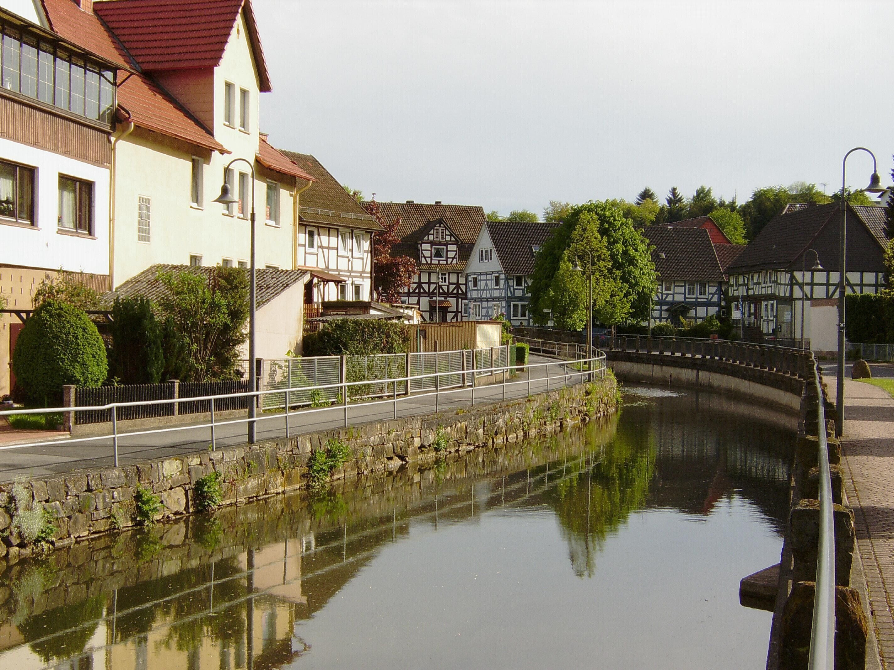 A canal with a stone bridge, traditional half-timbered houses, and a calm water surface reflecting the buildings.