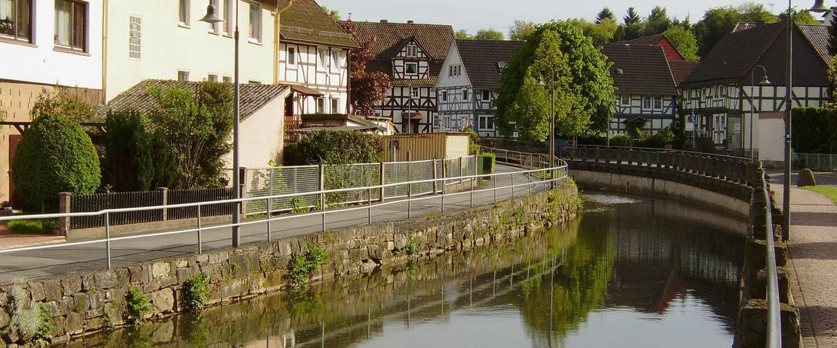A canal with a stone bridge, traditional half-timbered houses, and a calm water surface reflecting the buildings.