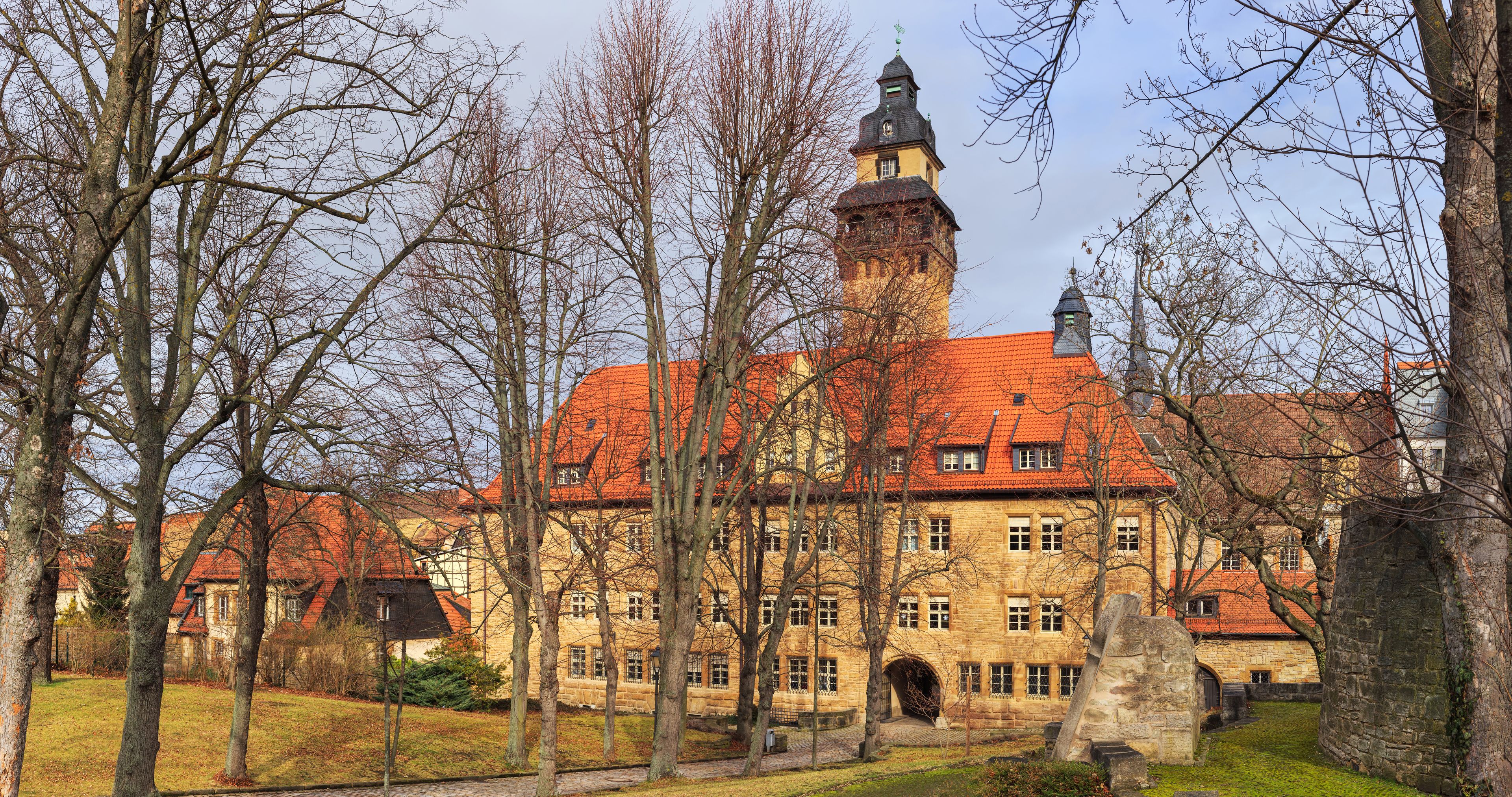 Ein historisches Gebäude mit rotem Ziegeldach, einem Turm und einer steinernen Fassade.