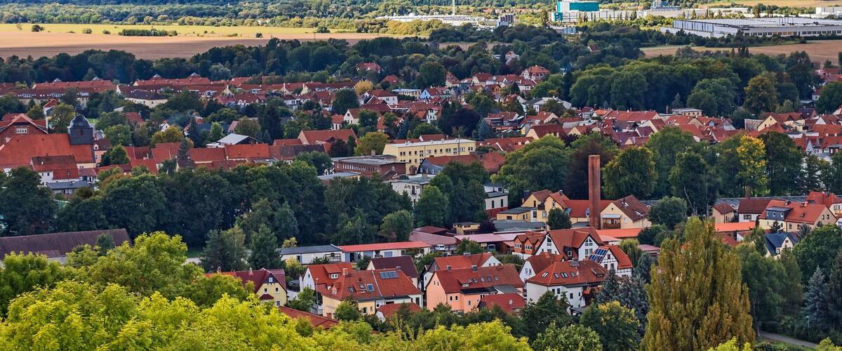 A town with red-roofed houses, green trees, and a distant industrial area.